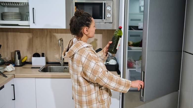 Woman reading the label on a bottle of cooking oil while standing in a kitchen