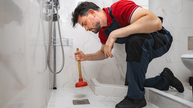 A man using a plunger to unblock a shower drain
