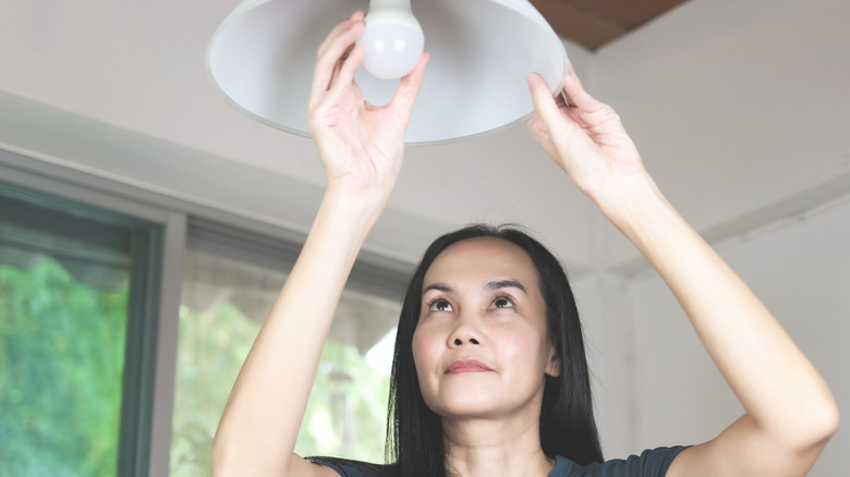 A woman replacing a lightbulb in a hanging fixture