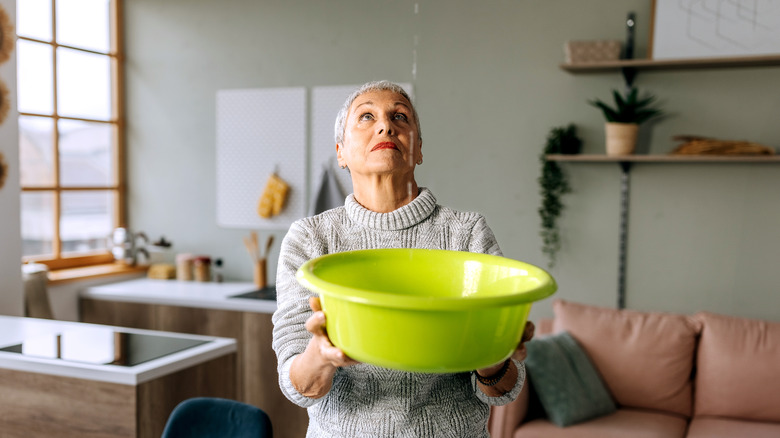 A woman catching water dripping from the ceiling in a plastic bowl