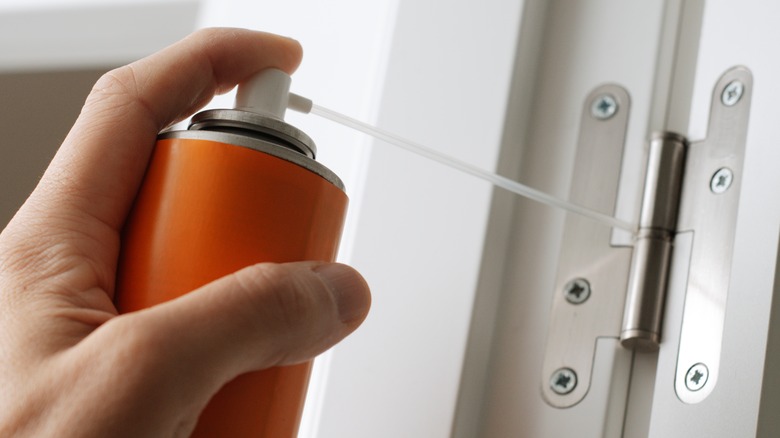 A hand spraying oil on a door hinge
