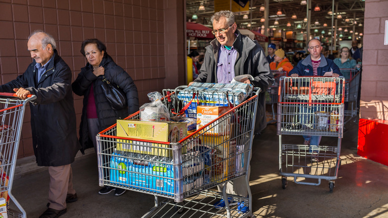 A group of costco shoppers exiting the store with full carts.