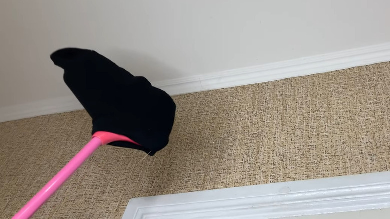 Black sock on a pink broom being used to sweep cobwebs from ceiling