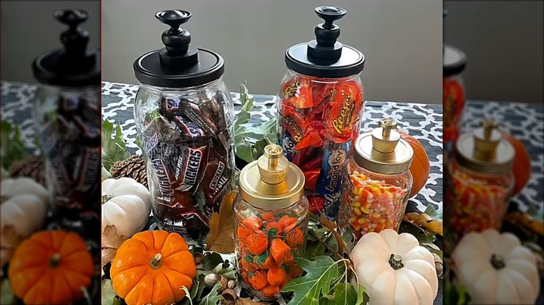 Upcycled pickle jars with intricate lids holding Halloween candy on a table