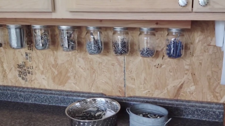 Upcycled glass jars attached to the underside of a cabinet to hold screws