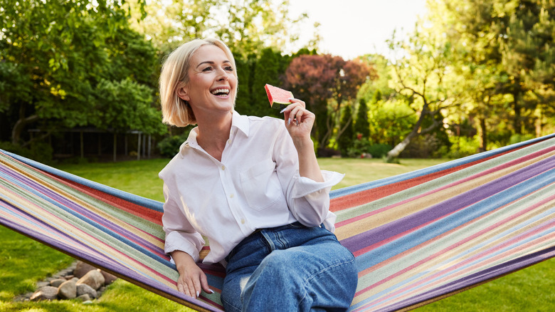 A person eating a watermelon slice on hammock amongst backyard trees
