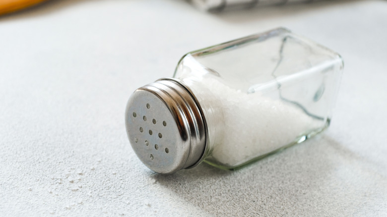 Spilled table salt in traditional glass jar on kitchen counter