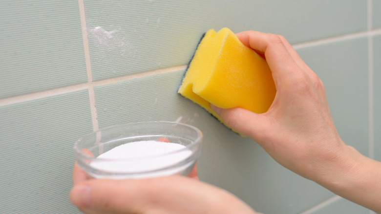 A hand cleaning tiles with a granulated substance from a dish