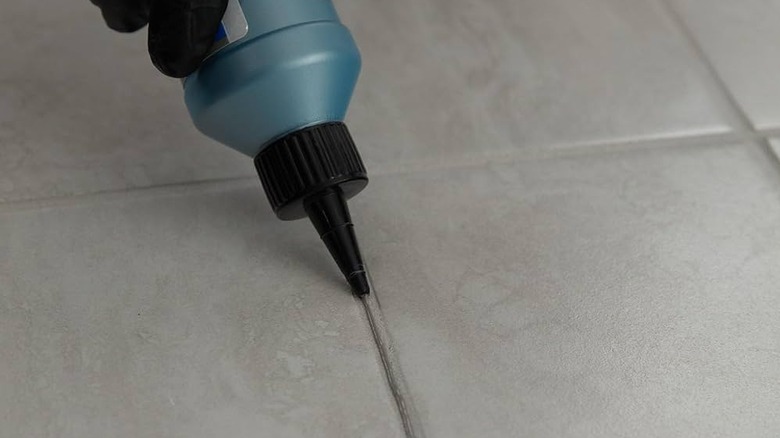 A hand applying a line of grout colorant/sealer to grout between tiles