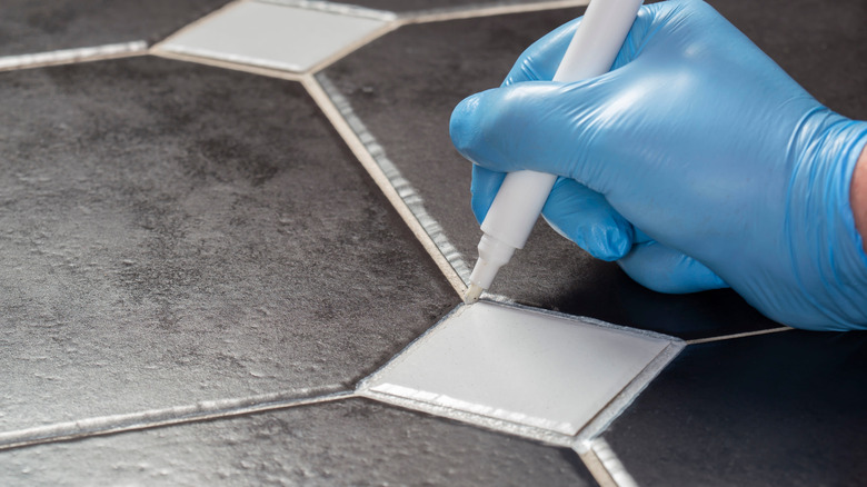 A gloved hand using a grout pen on tile grout