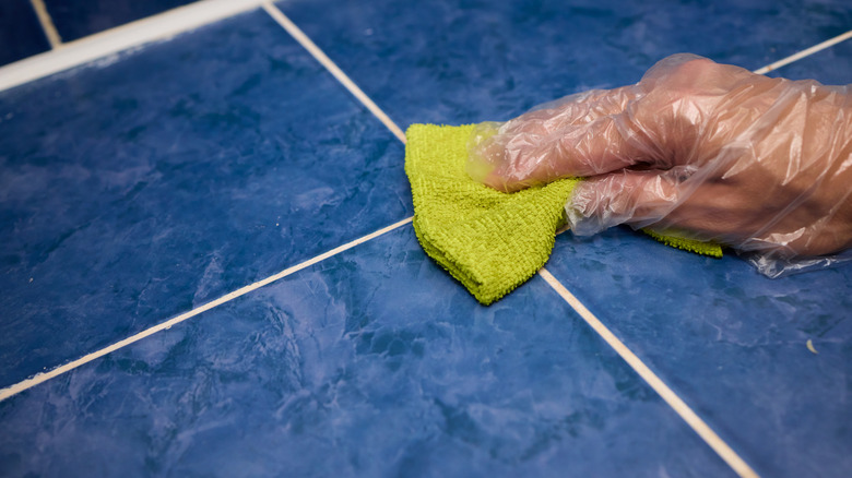 Close-up of a gloved hand cleaning white tile grout