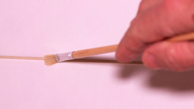 Close-up of a hand applying sealant to tile grout with a brush