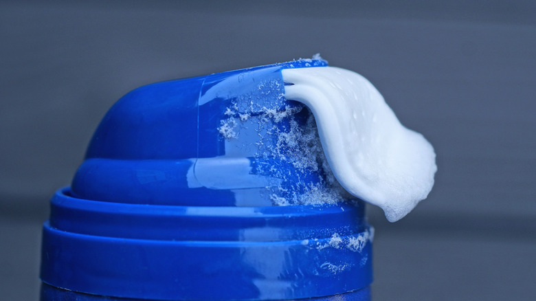 A close-up of a blue canister expelling shaving cream