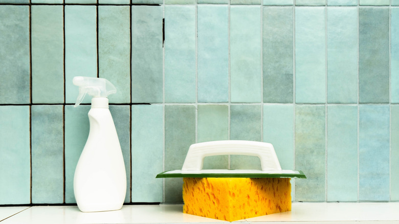 Cleaning supplies in front of a tiled wall with half dirty grout and half cleaned grout