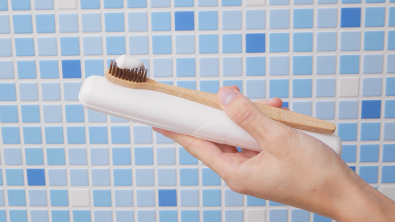 A hand holding a toothbrush with toothpaste on it in front of a tiled wall