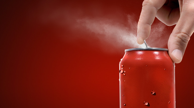 Hand opening a red soda can