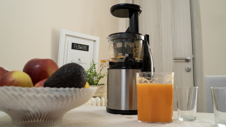 A juicer, some fruit, and a fresh glass of juice.