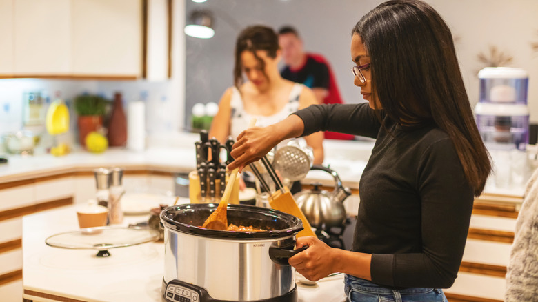 A woman stirring food in a Crock-Pot.
