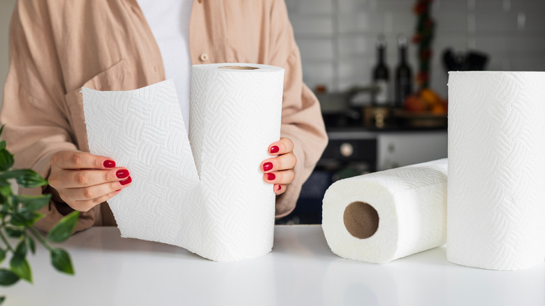 hands taking a paper towel off the roll and two other paper towel rolls on counter