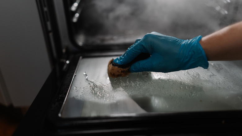 person cleaning oven door with steam in background