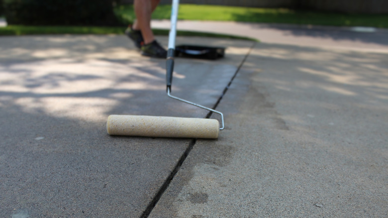Someone using a roller to seal a concrete driveway