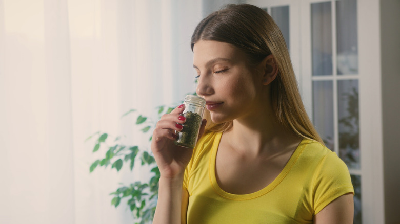 Woman smelling bottle of dried cooking herbs