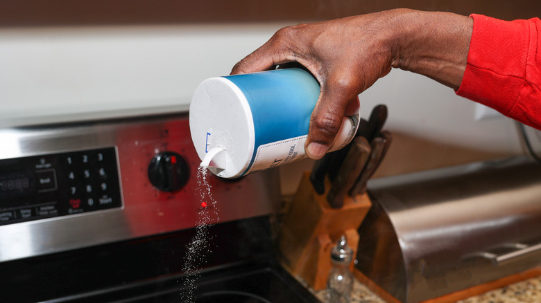 person pouring salt on stove