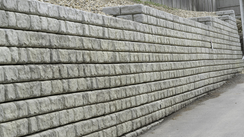 A large gray retaining wall preventing soil collapsing onto a driveway