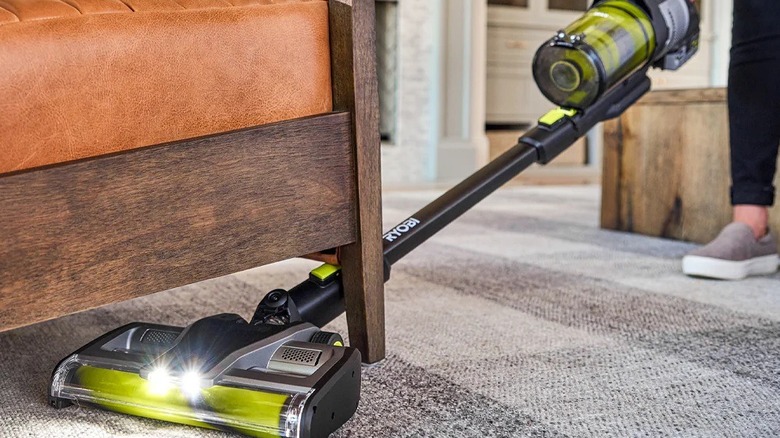 Person using a Ryobi stick vacuum under furniture