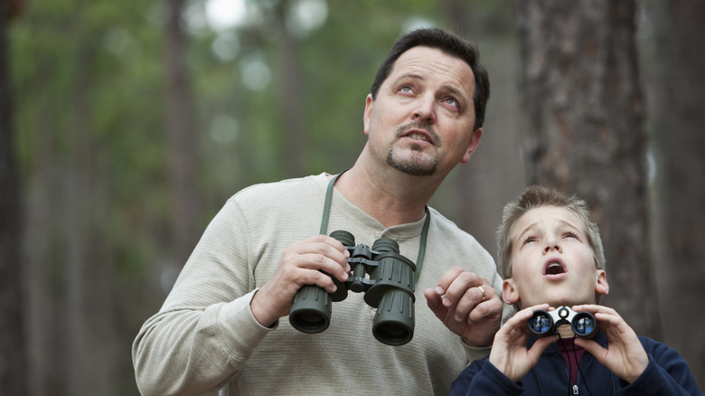 A man and his son are both holding binoculars and looking up