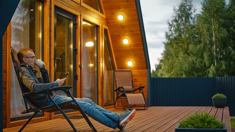 A man sits on his deck lounger in the evening, with yellowish outdoor lights turned on