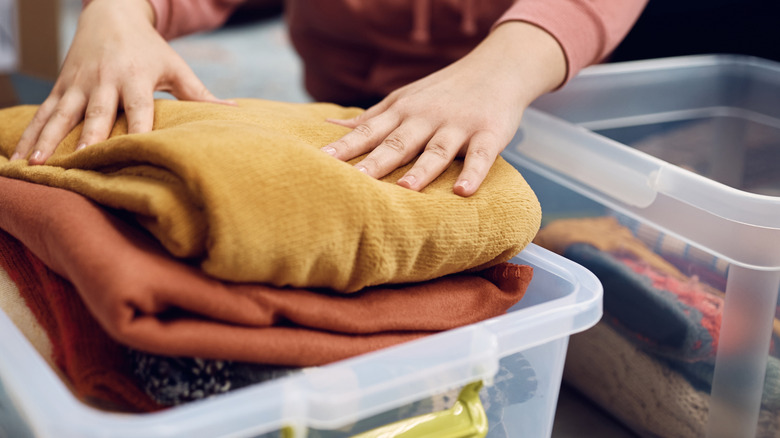 A woman packing clothes into a plastic box