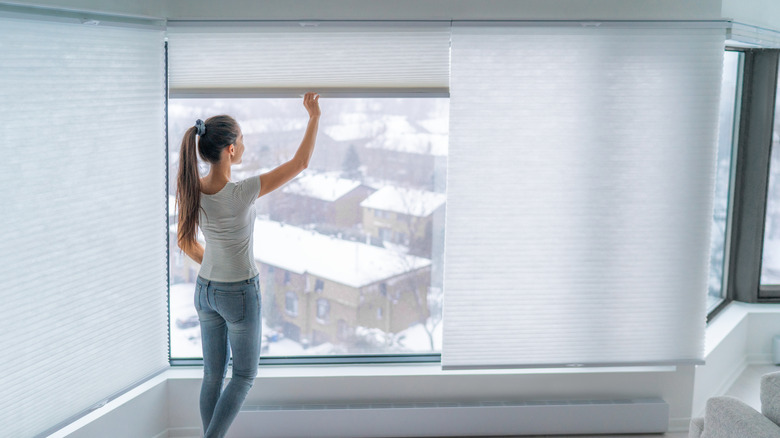 A woman pulls down accordion blinds in her apartment.
