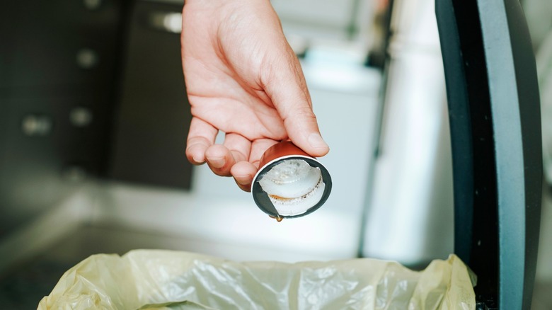 person emptying used coffee pod in trash can