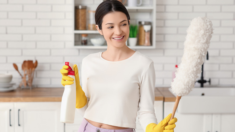 Woman holds spray bottle and duster to use together.