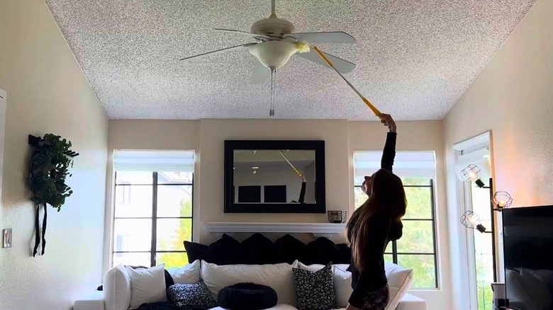 Woman reaches tall light with Swiffer Extendable Duster.