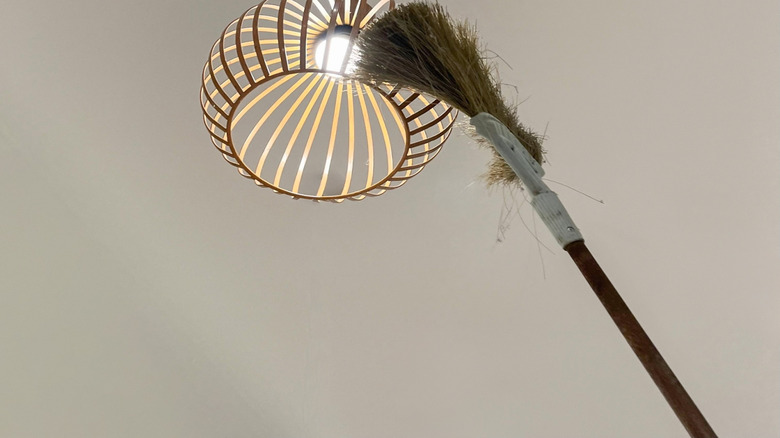 A broom cleans off a light fixture.