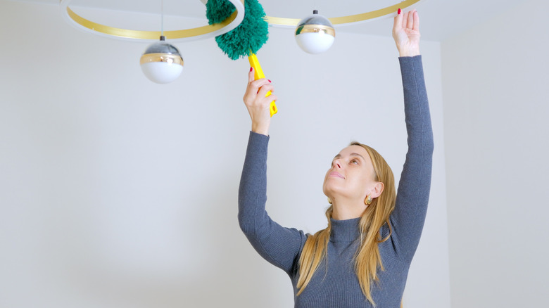 woman reaching up to dust a ceiling light fixture