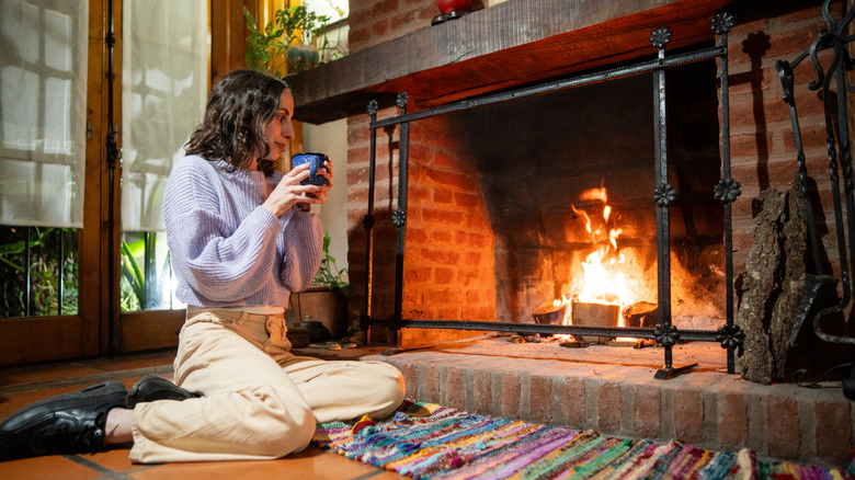 Woman feeling cozy by a lit brick fireplace