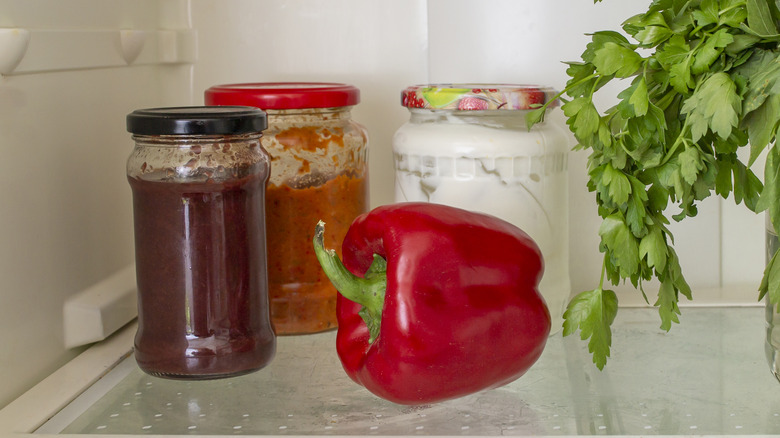 A red pepper and jars in a refrigerator