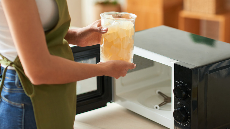 A woman in a green apron placing a jar into a microwave