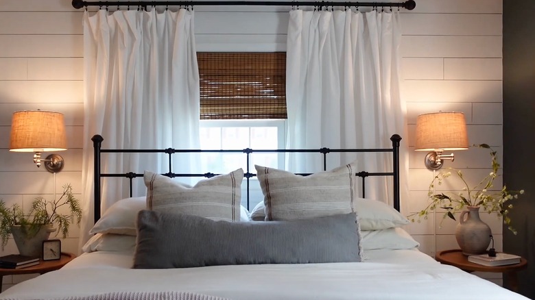 Bed in front of window with curtain panels and a shade