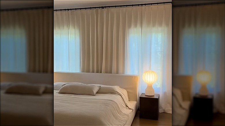 A bed in front of a large wall of windows with floor to ceiling curtains covering the entire wall behind the bed