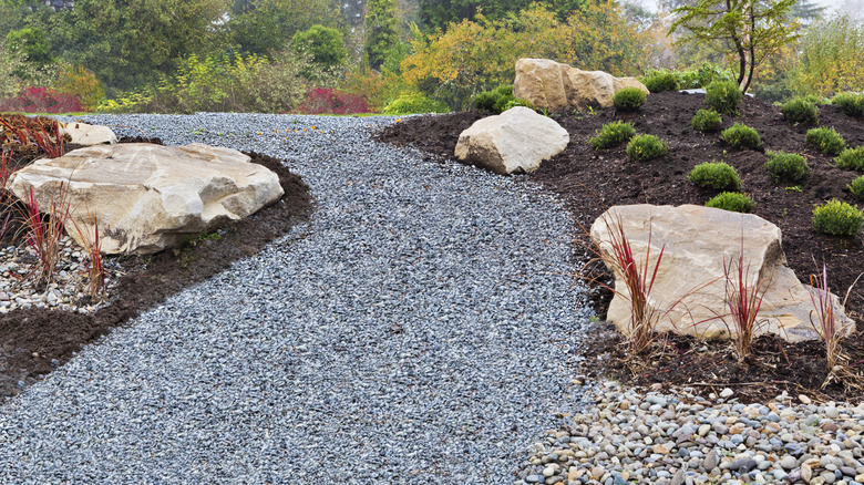 A gravel path winds between two garden plots in a backyard