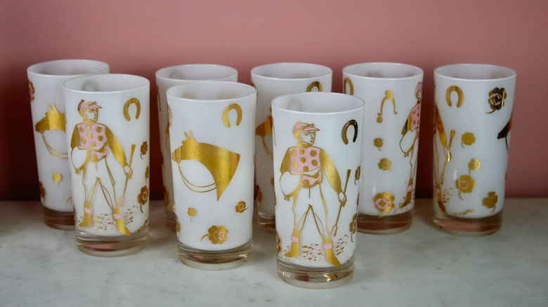 A set of Fred Press Highball Glasses featuring a Jockey Horse design in pink and gold sits on a marble countertop