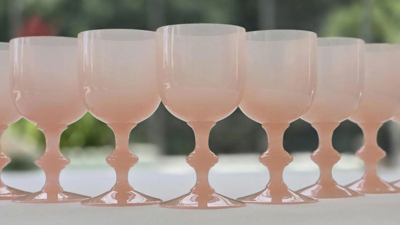A row of Portieux Vallerysthal Soft Pink Opaline Cordial Apertif Digestif Glasses sits on a table outside