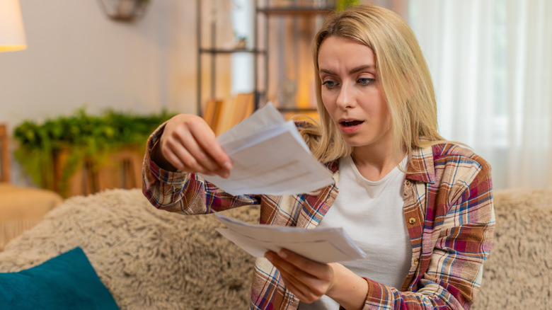 A woman looks at a bill with a surprised look on her face.