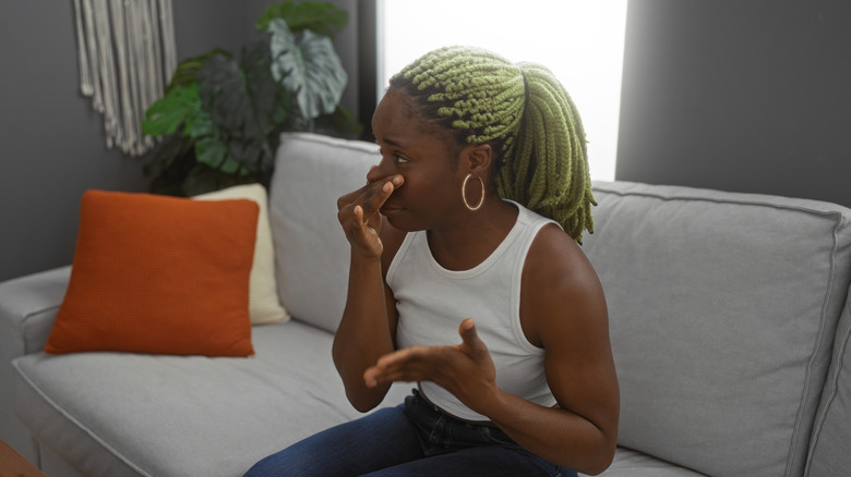 A woman sitting on a couch holds her nose in reaction to a bad smell.
