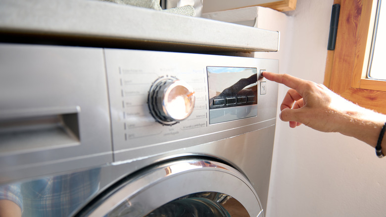 Hand hitting a button on a dryer or washing machine