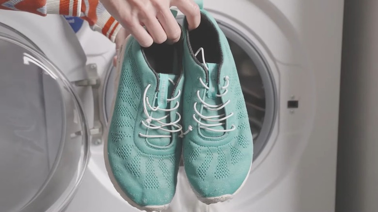 Person holding a pair of blue-green tennis shoes in front of a dryer